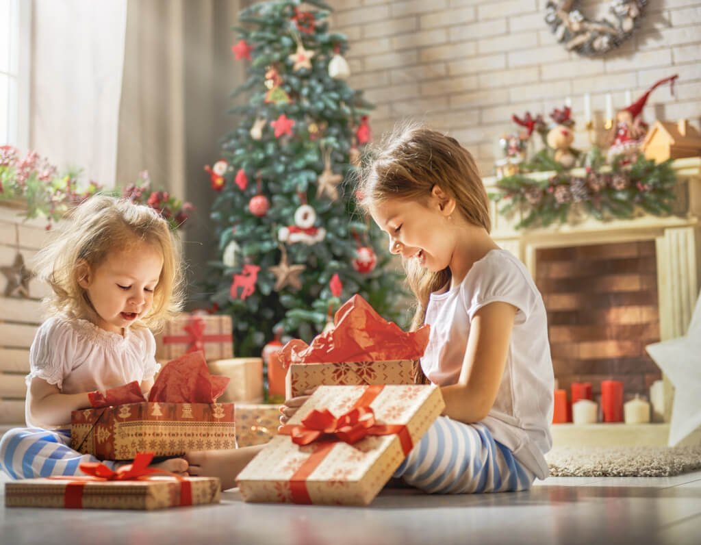 Merry Christmas and Happy Holidays! Cheerful cute childrens girls opening gifts. Kids wearing pajamas having fun near tree in the morning. Loving family with presents in room.