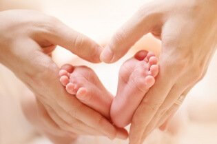 Baby feet in mother hands. Tiny Newborn Baby's feet on female Heart Shaped hands closeup. Mom and her Child. Happy Family concept. Beautiful conceptual image of Maternity