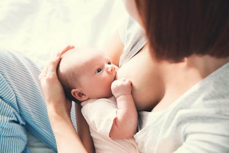 Mother breastfeeding baby in her arms at home. Beautiful mom breast feeding her newborn child. Baby eating mother's milk. Young woman nursing and feeding baby. Concept of lactation infant.