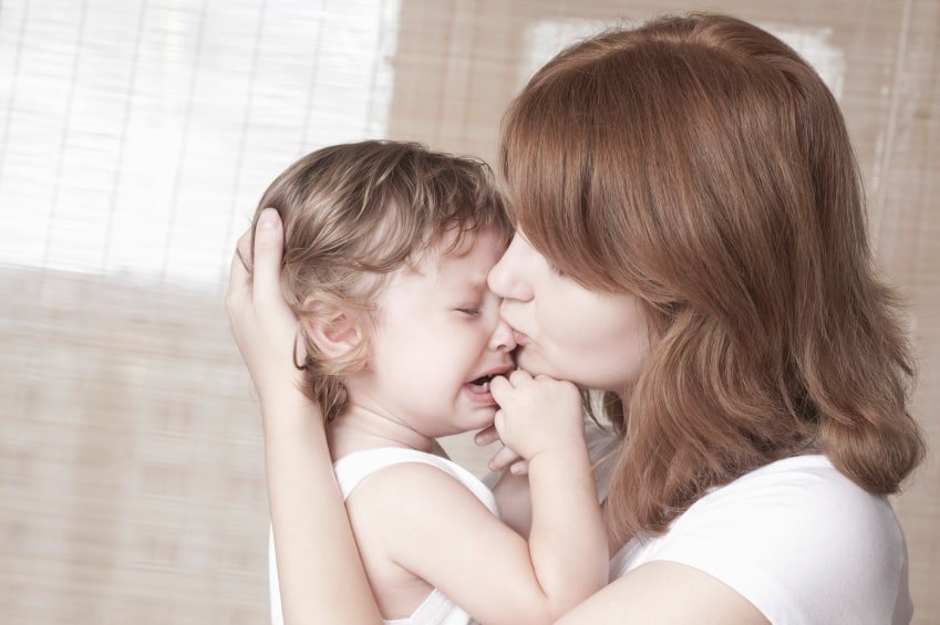Side view of young mother comforts crying baby girl