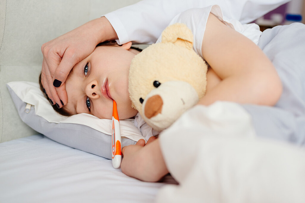 Sick baby boy in bed with a thermometer under his arm