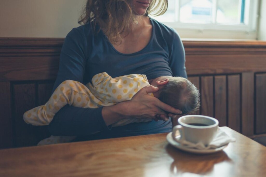 woman-breast-feeding-in-front-of-coffee-mug-in-cafe